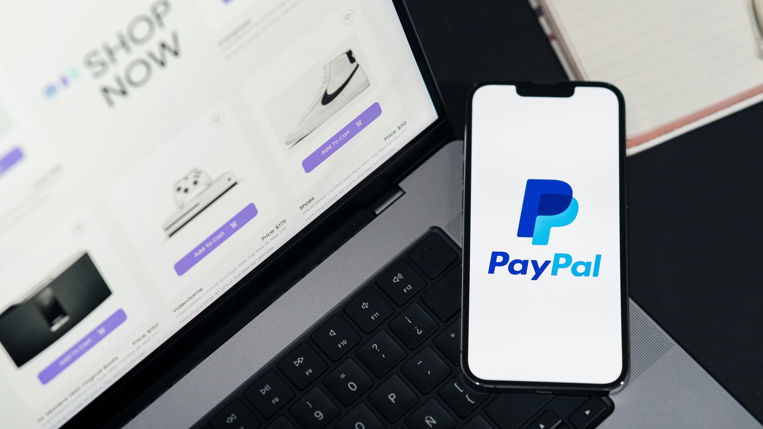 Smartphone displaying PayPal logo next to laptop with online shopping site open.